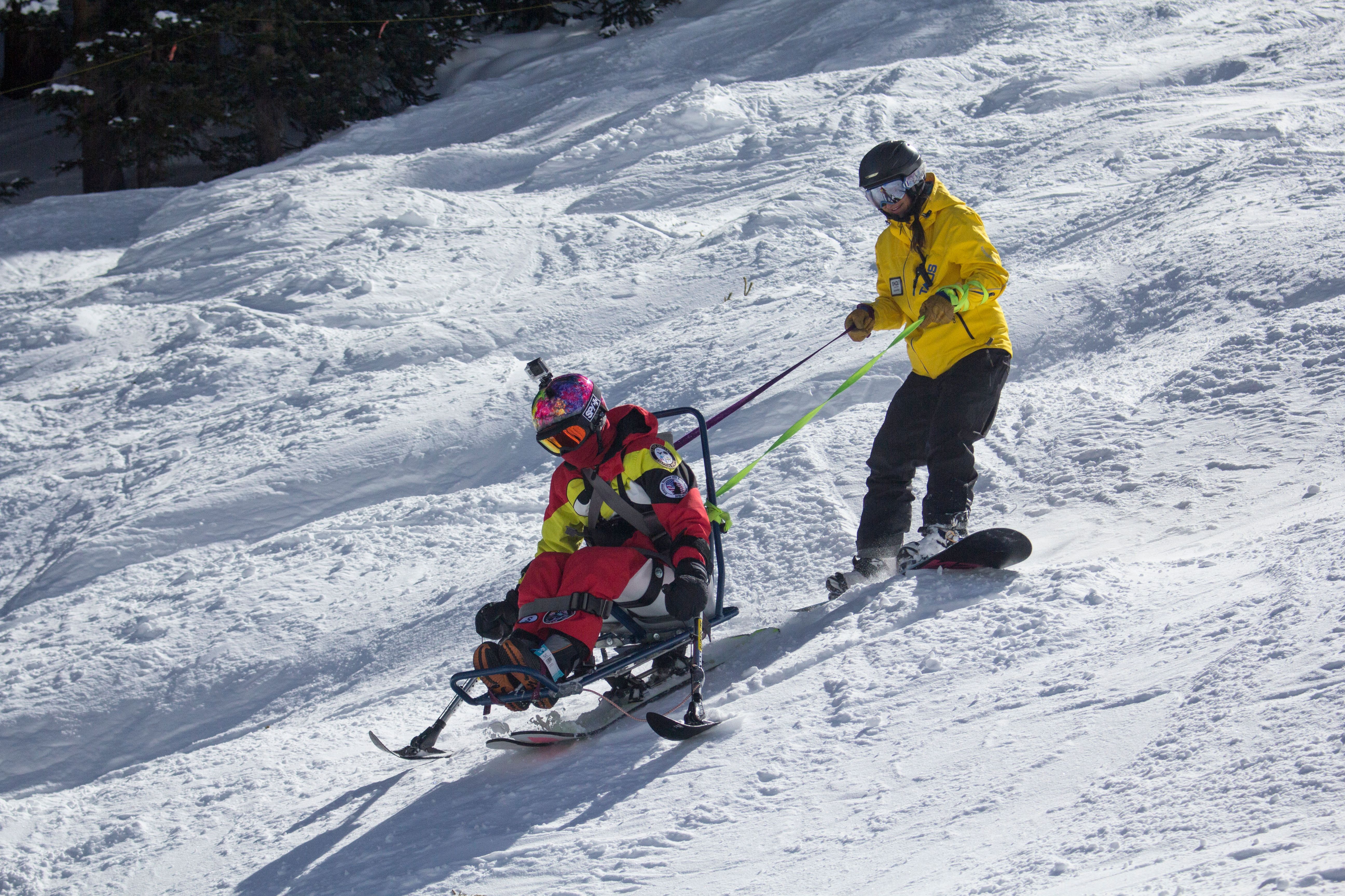A ski instructor teaching a student how to ski on a sit ski